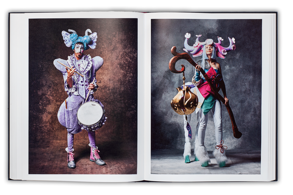 Mayflies book spread, left page: Carnvalist with blue hair and pink outfit with a snare drum twirling a drumstick, right page centaur cosplayer with pink antlers