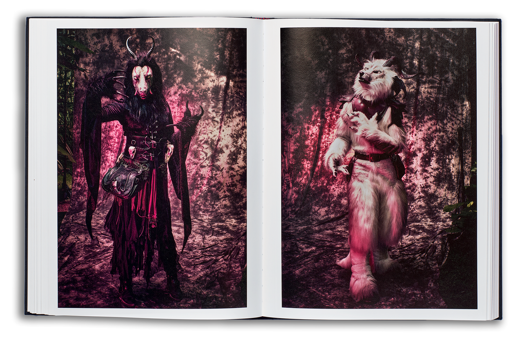 Mayflies book flat spread, left page: Demoness furry with black robes, long animal claws and horns, and a white face with tusks looking directly to camera, right page: A fox demon furry with white fur and black horns, looking dreamily off to camera left
